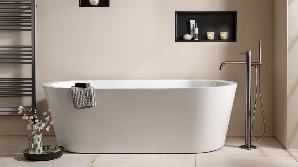 A modern style bathtub in white sits in a minimalist bathroom decor; a free standing tap sits to the right.